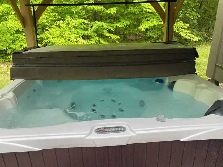 A hot tub with a cover, surrounded by a wooden deck and lush greenery