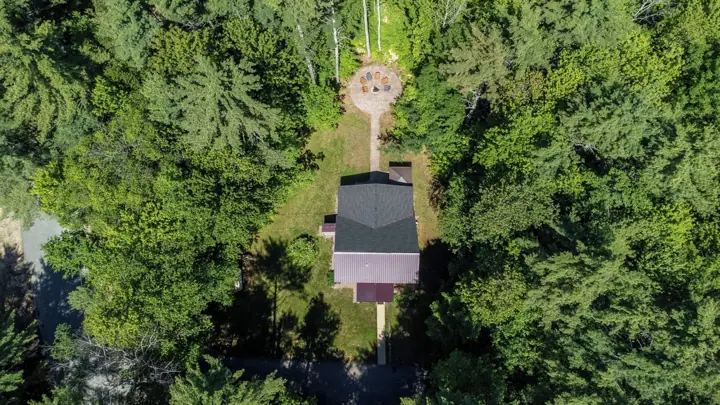 An aerial view of a house surrounded by dense forest, with a visible patio area and a distinct roof structure