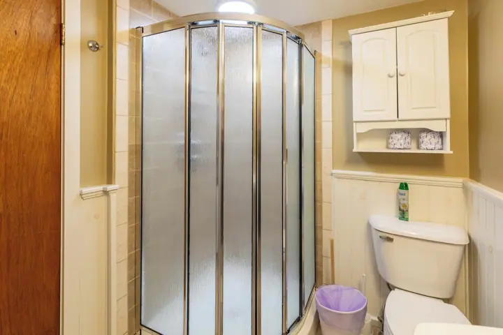 A bathroom with a glass shower enclosure, a white toilet, and a cabinet above the toilet