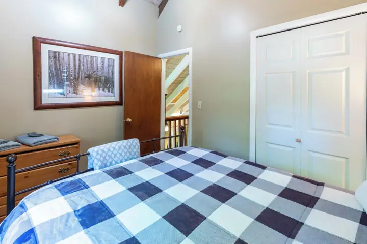 A bedroom with a checkered bedspread, a wooden dresser, a framed picture on the wall, and a white door