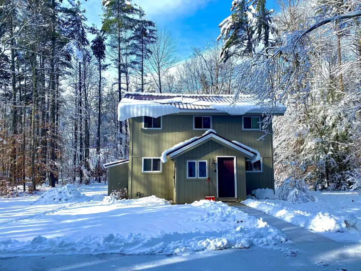A two-story cabin with a snow-covered roof, surrounded by a forest