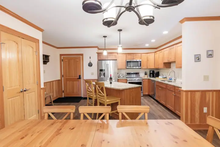 A kitchen with wooden cabinets, a stainless steel refrigerator, a microwave, and a dining area with a wooden t