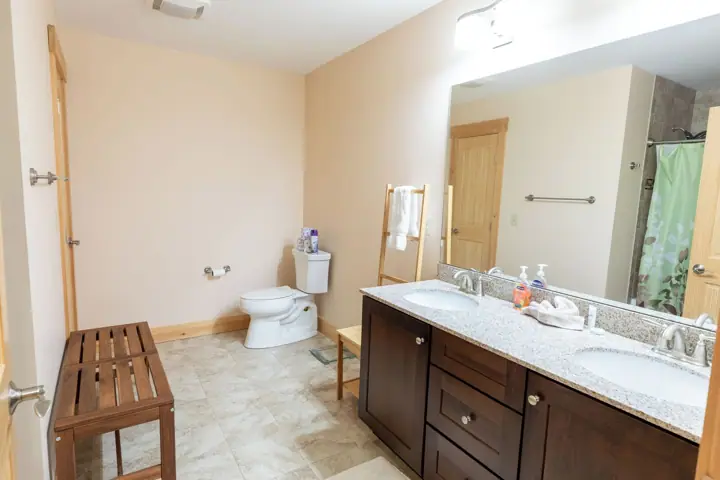 A bathroom with a wooden bench, a toilet, a sink, and a shower area