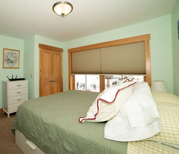 A bedroom with a bed, a wooden door, a window with blinds, and a white dresser