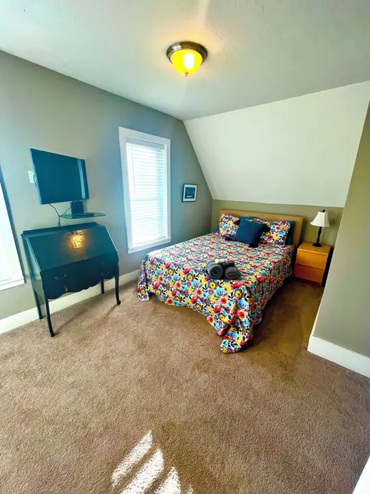 A bedroom with a bed, a desk, a TV, and a window