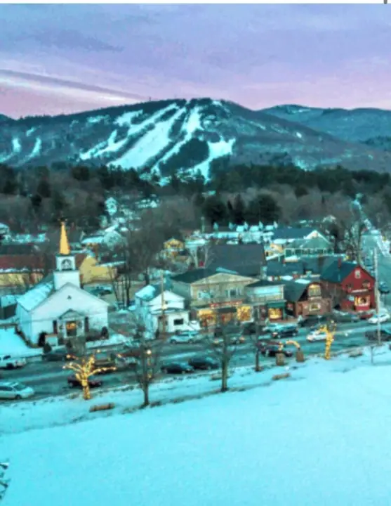 A town with buildings, a church, and snow-covered mountains in the background