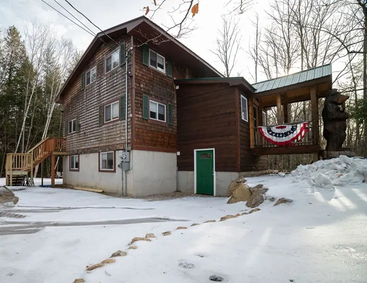 A wooden cabin with a green door, a covered porch, and a flag