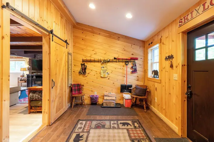 A wooden interior with a sliding door, a wall-mounted coat rack, a welcome sign, and a ski-themed rug