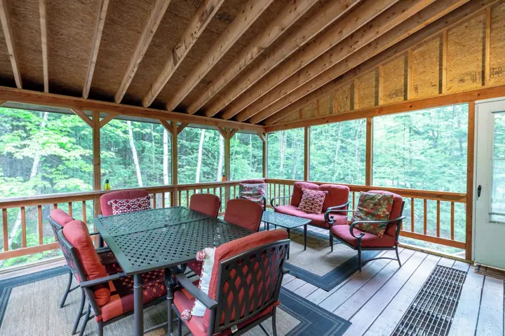A covered outdoor deck with wooden beams, a table, and red upholstered chairs