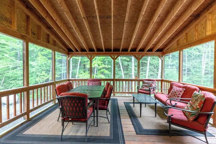 A covered outdoor deck with a table and chairs, surrounded by a wooden railing