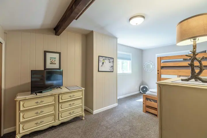A room with a television on a dresser, a bed with a wooden headboard, and a ceiling fan