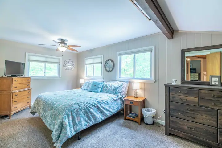 A bedroom with a bed, dresser, vanity, and a ceiling fan