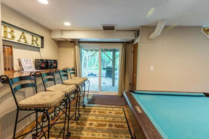 A pool table, a bar area with a sign, and a seating area with chairs