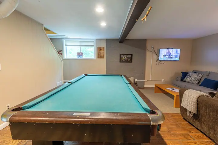 A pool table in a room with a sofa, a television, and a window