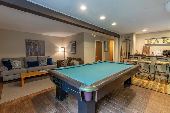 A pool table in a room with a sofa, a lamp, and a bar area