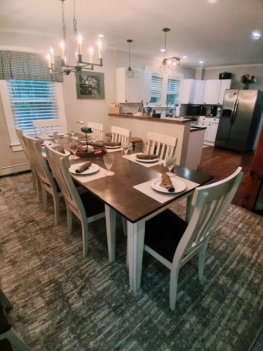 A dining area with a wooden table set for six, surrounded by white chairs with cushioned seats