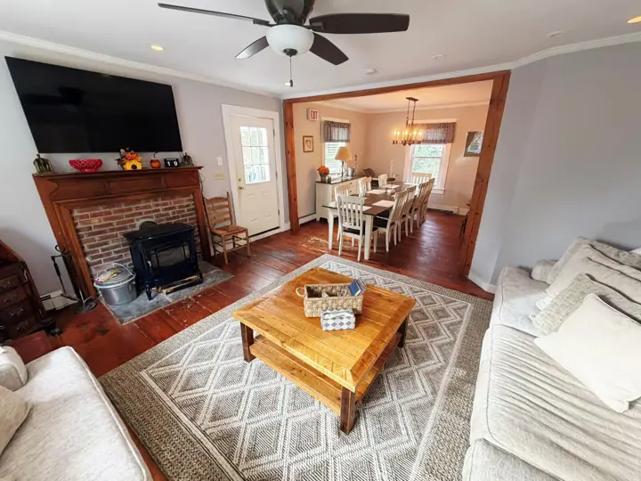 A living room with a fireplace, a dining area, and a ceiling fan