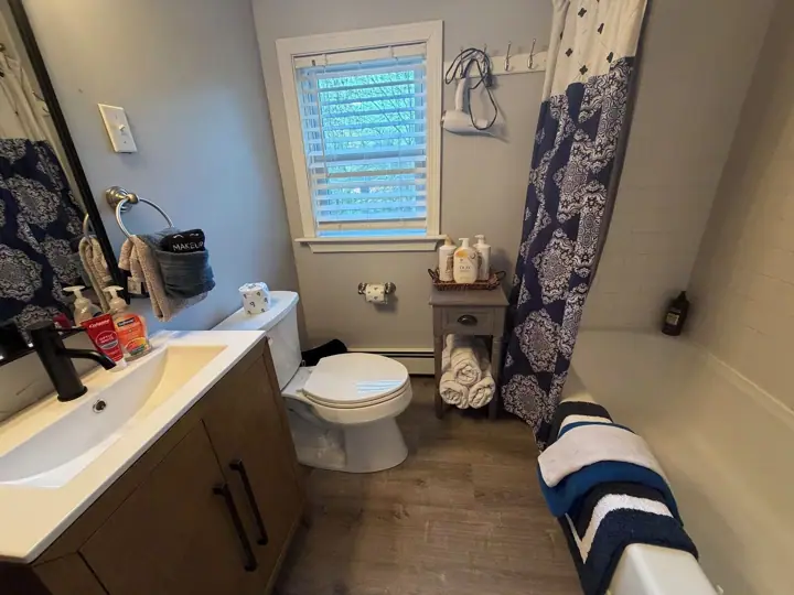 A bathroom with a toilet, sink, mirror, and a window with blinds