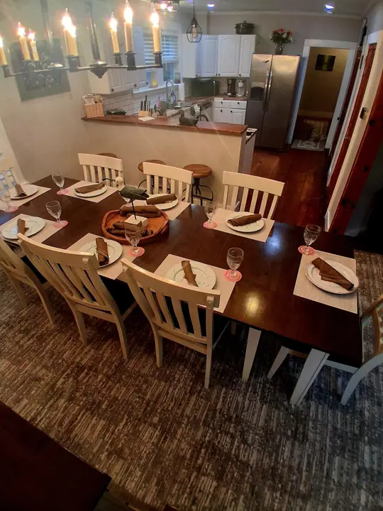 A dining area with a wooden table set for six, surrounded by white chairs