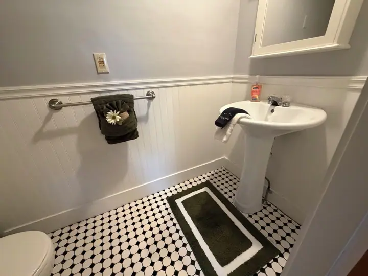 A bathroom with a toilet, a sink, a towel rack with a towel, a patterned floor, and a mirror above the sink