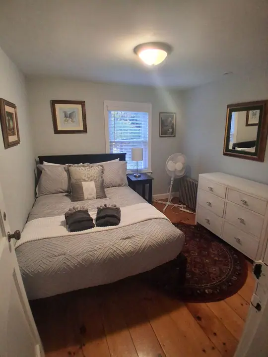 A bedroom with a bed, dresser, and a standing fan