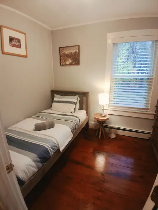A small bedroom with a single bed, a nightstand, a window with blinds, and two framed pictures on the wall