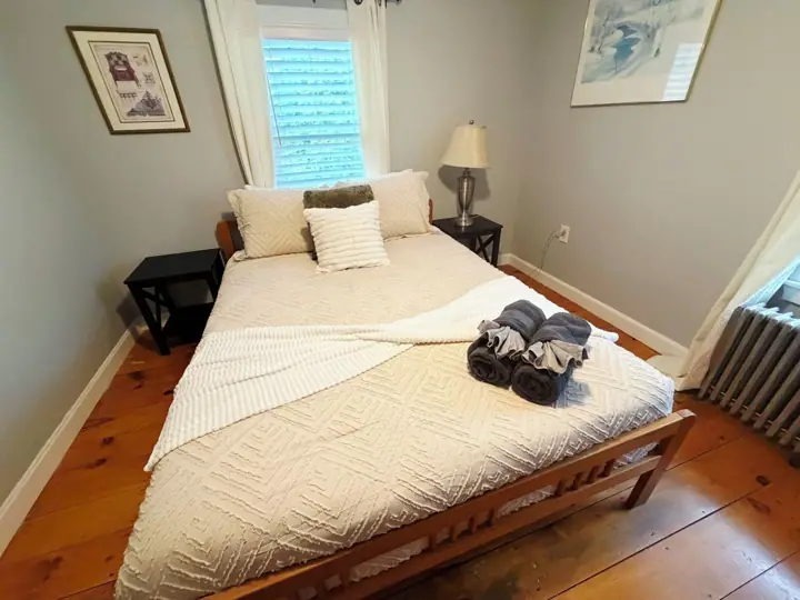 A neatly made bed with a white quilt, a wooden headboard, and a bedside table with a lamp