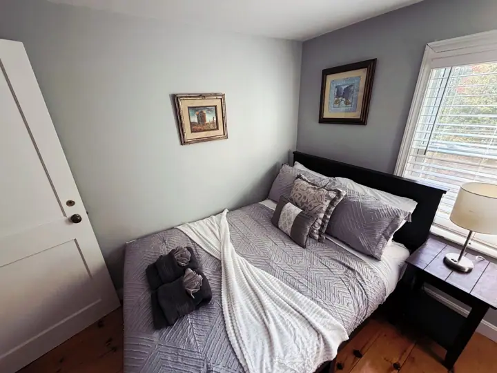 A bedroom with a bed, a nightstand, a lamp, and two framed pictures on the wall