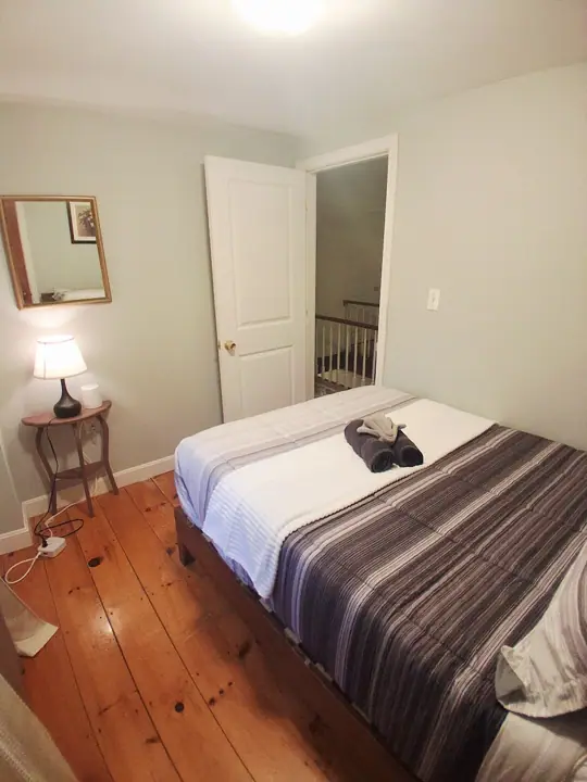 A bedroom with a bed, a nightstand with a lamp, a door leading to a balcony, and a mirror on the wall