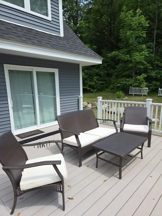 A deck with wicker furniture and a house in the background
