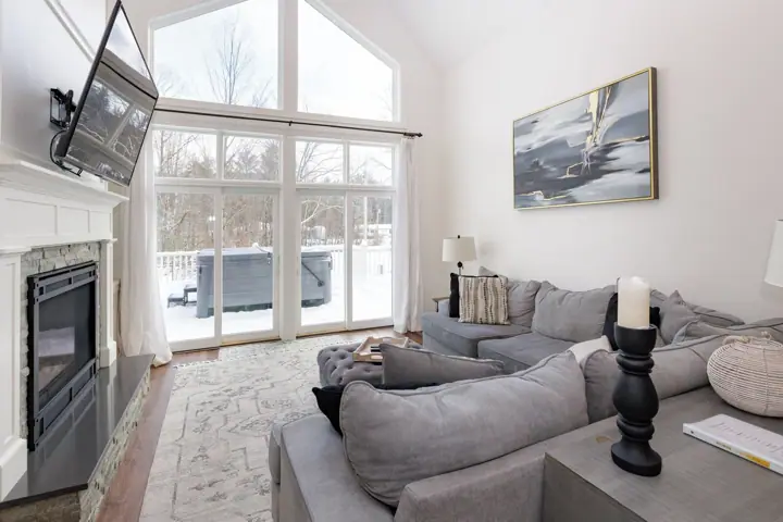 A living room with a fireplace, grey sofas, a large window, and a painting on the wall