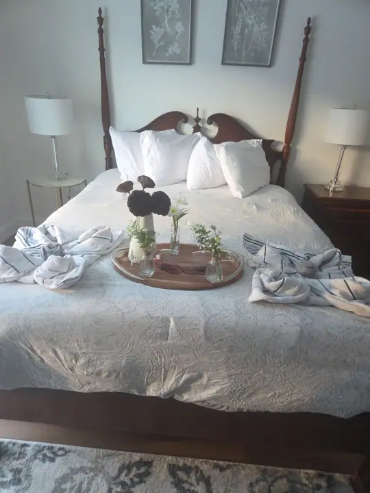 A neatly made bed with a wooden headboard, white pillows, and a tray with flowers and a candle. There are two 