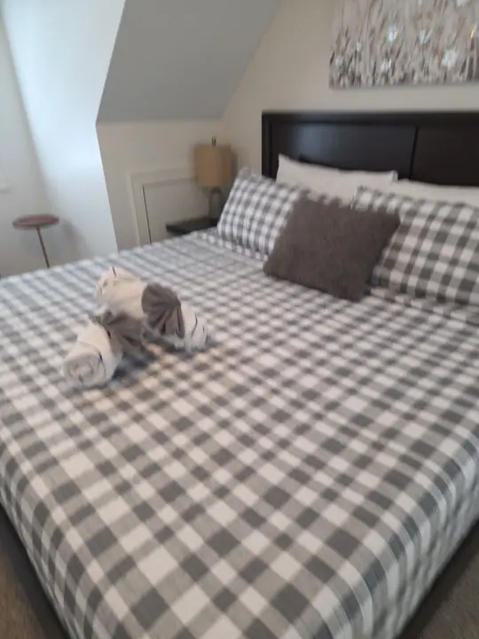 A neatly made bed with a checkered bedspread, a pillow, and a folded towel on the floor