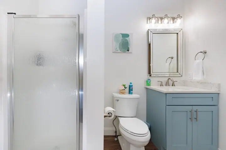 A bathroom with a glass shower door, a toilet, a sink with a mirror above it, and a towel rack