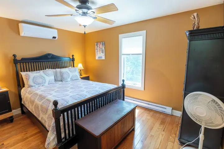 A bedroom with a bed, a ceiling fan, an air conditioner, a window, and a fan on a stand