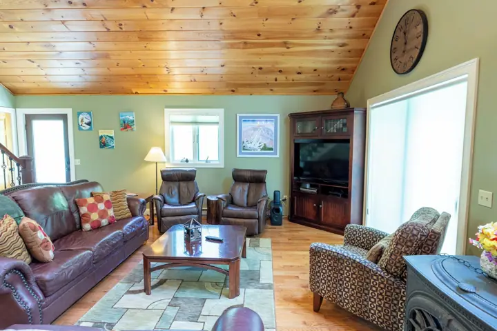 A living room with a wooden ceiling, leather sofas, a coffee table, a fireplace, and a television