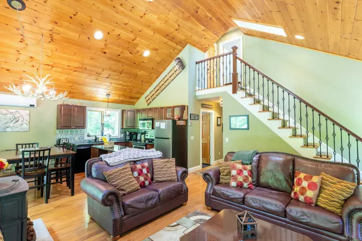 A spacious living area with a wooden ceiling, two leather sofas, a dining table, and a staircase leading to an
