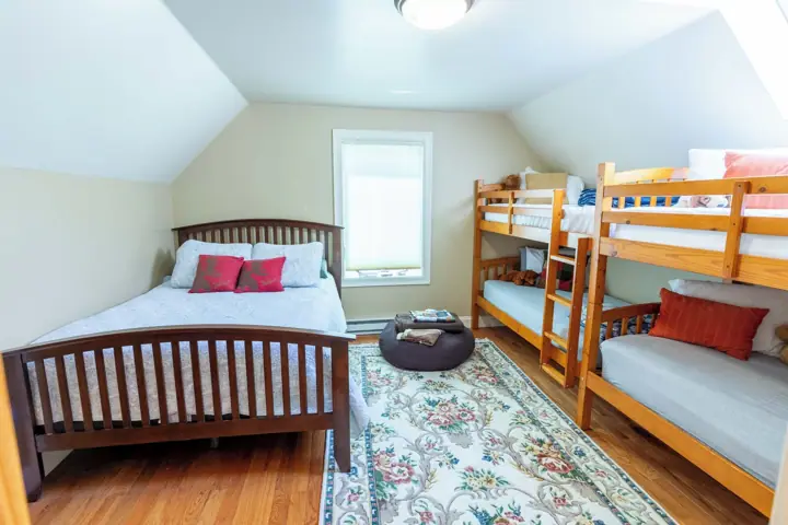A dorm-style room with bunk beds, a single bed, a window, and a patterned rug