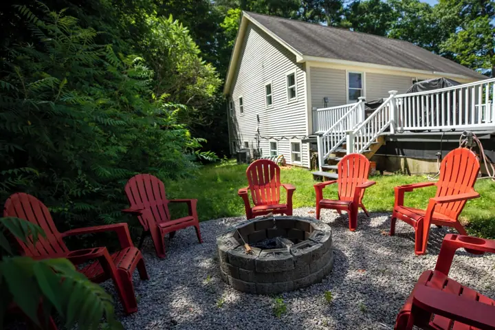 A house with a deck, a fire pit, and red Adirondack chairs