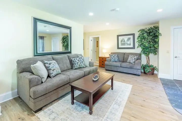 A living room with two grey sofas, a wooden coffee table, a large mirror, a framed picture, and a potted plant