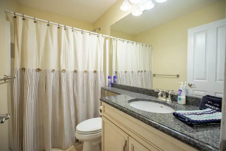 A bathroom with a shower curtain, toilet, sink, mirror, and toiletries