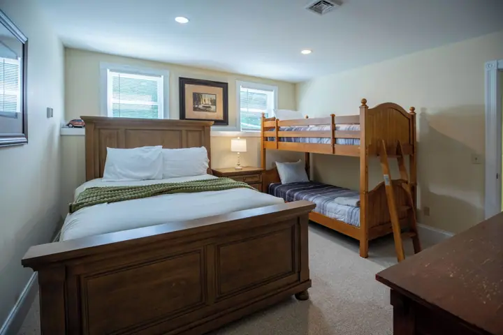 A bedroom with a large bed, a smaller bunk bed, a nightstand with a lamp, and a framed picture on the wall