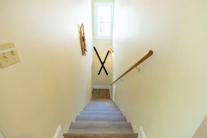 A staircase with wooden steps, a handrail, and a wall-mounted light fixture