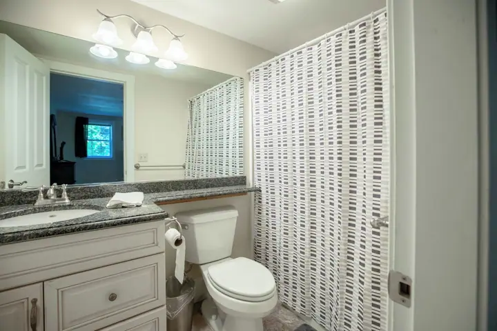 A bathroom with a white toilet, a sink with a mirror above it, and a shower curtain with a geometric pattern