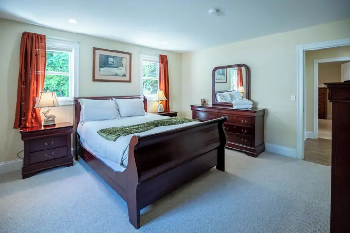 A bedroom with a large bed, a dresser, a mirror, and a window with curtains