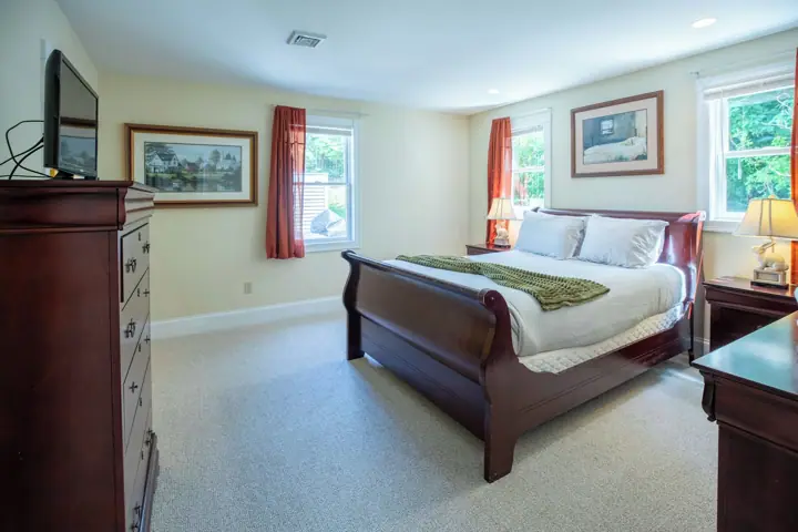 A bedroom with a bed, dresser, and two windows with curtains
