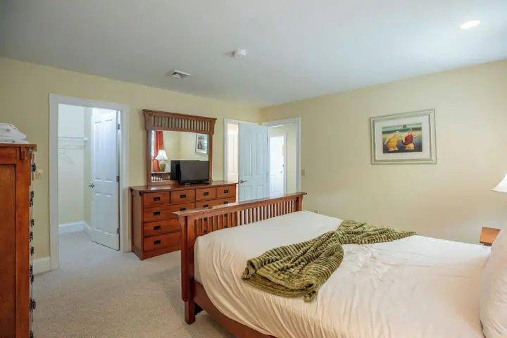 A bedroom with a bed, dresser, television, and a painting on the wall