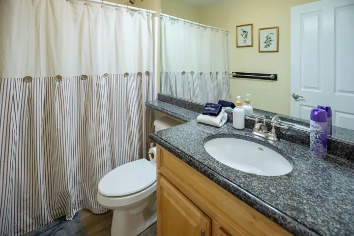A bathroom with a striped shower curtain, a white toilet, a granite countertop sink, and a mirror