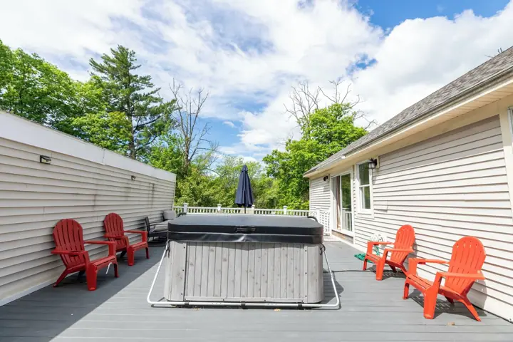A deck with a hot tub, red Adirondack chairs, and a white fence