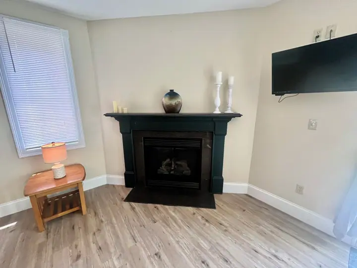 A room with a fireplace, a TV mounted on the wall, and a window with blinds